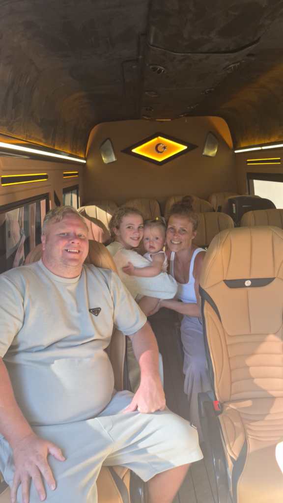 Dört kişilik bir aile, lüks bir aracın içinde gülümseyerek poz veriyor. Arkada sarı ve kahverengi tonlarında tasarlanmış koltuklar görünmekte.
